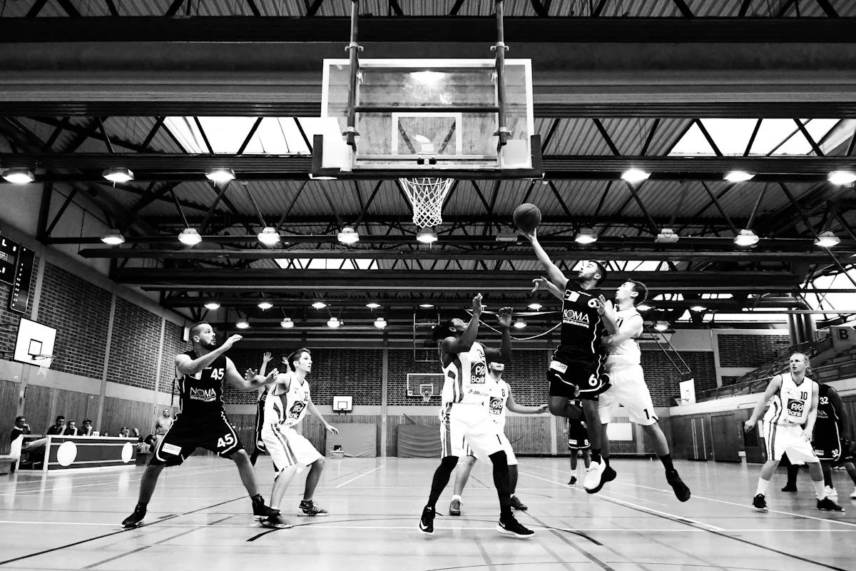 Partido de baloncesto en una pista cubierta, fotografiado en blanco y negro.